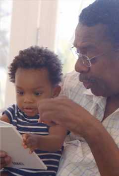 Grandfather shares a book with a smiling toddler.