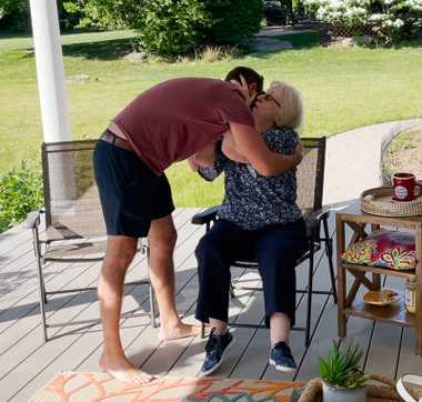 Adult son bear hugs his mother as she kisses his cheek.
