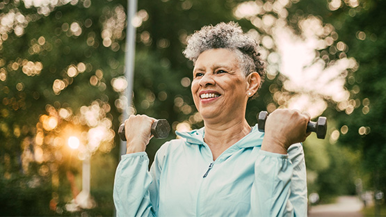 A woman smiles, lifting weights outdoors